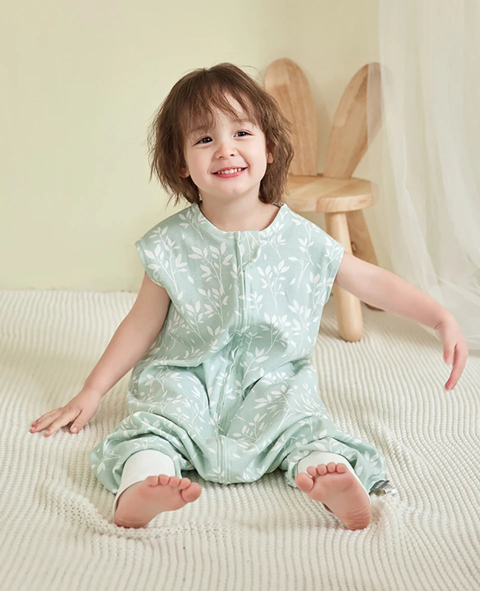 Enfant souriant assis en tailleur portant la gigoteuse à pied vert sauge