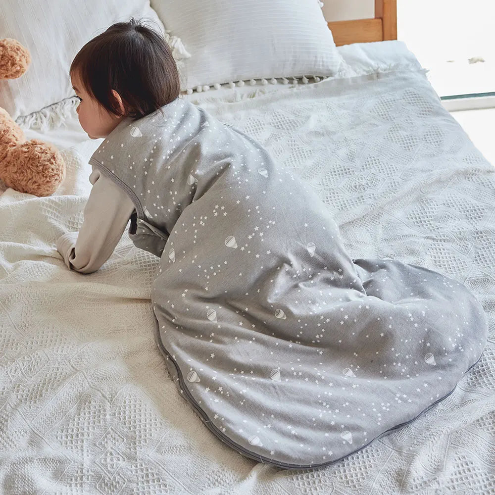 Bébé à quatre pattes portant la gigoteuse grise sur un lit
