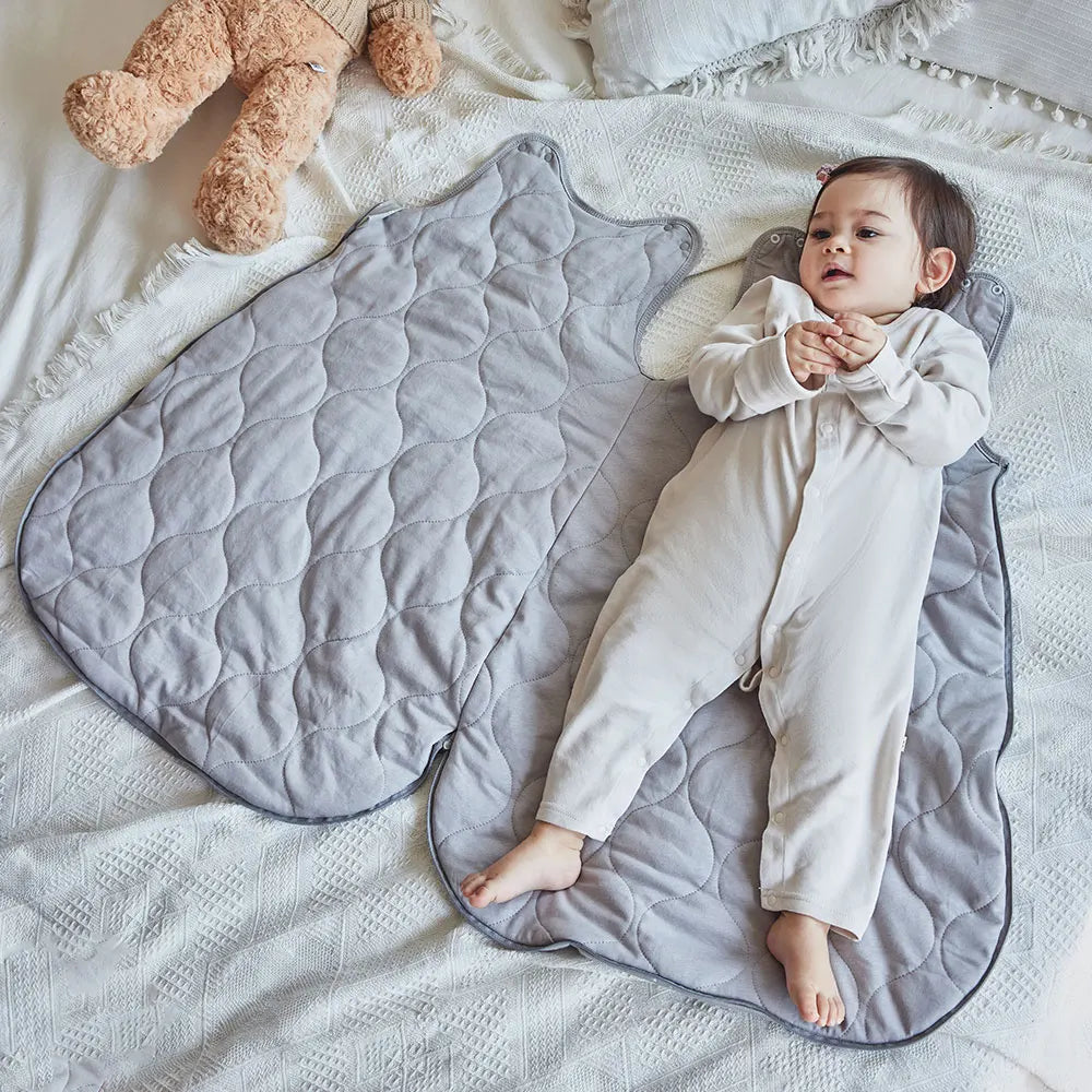 Bébé allongé sur la gigoteuse ouverte posée à plat, matière matelassée grise